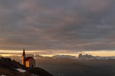Latzfonser cross chapel at sunrise with clouds and South Tyrolean mountains