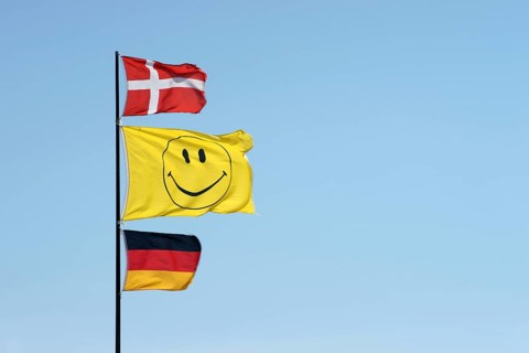 German and Danish flags waving together with a smiley flag on a flagpole