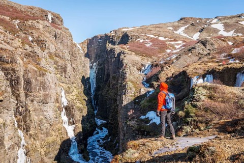 Man in orange jacket standing at the canyon of Glymur Waterfall
