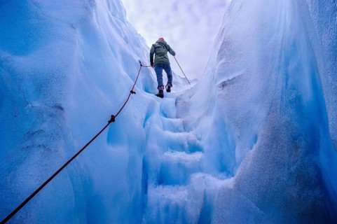 Woman walking steps out of a ice cave in Fox Glacier