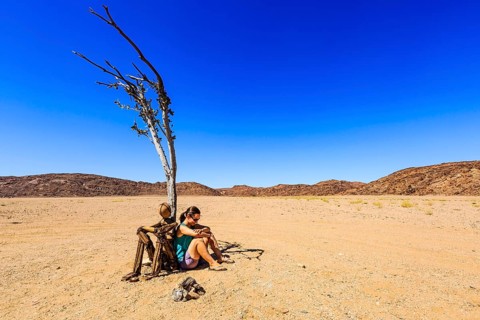 Young woman sitting under a dried tree next to a cairn Lonely Man