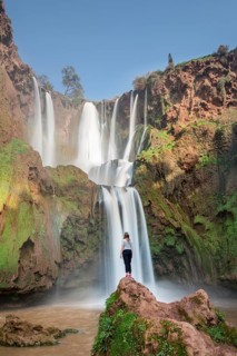 Young woman standing on a stone in front of Ouzoud waterfalls and cascades