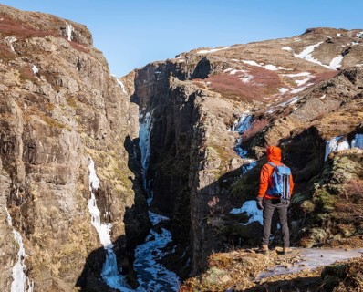 Man in orange jacket standing at the canyon of Glymur Waterfall