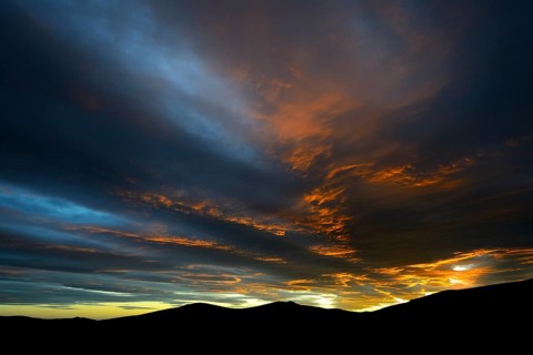 Dramatic sunset with rising storm clouds in front of mountain silhouette