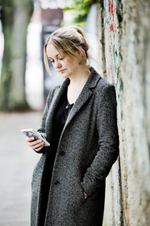Young woman leans against a wall and looks at her smartphone