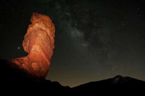 Illuminated Roque Cinchado in front of Pico del Teide with starry sky