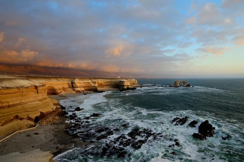 Rocky coast with arch La Portada at sunset with clouds