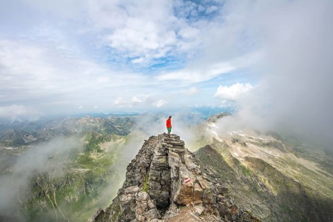 Hiker on the summit of the Hochgolling with rising fog