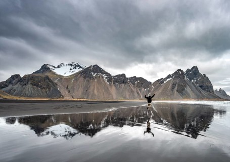 Hiker jumps at the black sandy beach