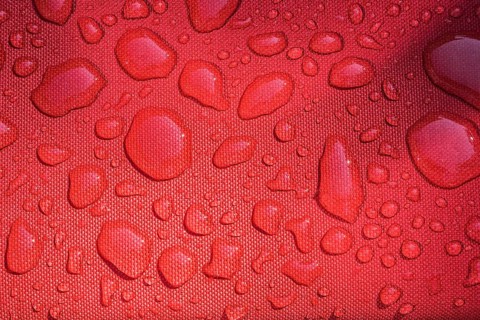 Close-up of raindrops on surface of water resistant red canvas material