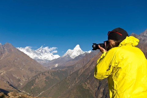 Photographer with yellow jacket taking a photograph of Mount Everest Mountain