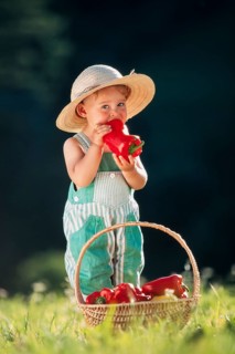 Three-year old girl with straw hat biting into a pepper