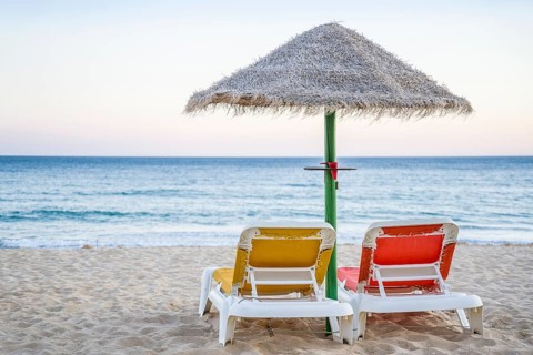 Colorful red and yellow sun beds under straw umbrellas on Falesia Beach