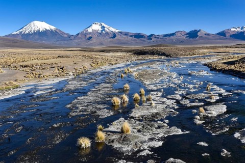 Snow-covered volcanoes Pomerape and Parinacota with icy river