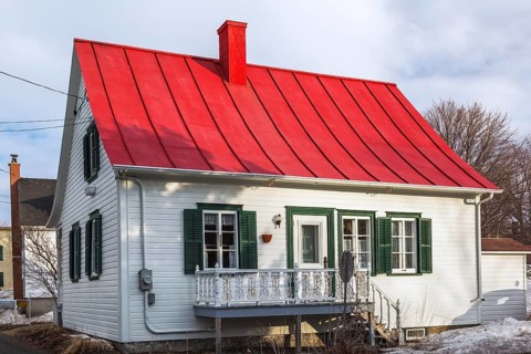 Rear of old 1835 white wood plank with green trim Canadiana cottage style house with red sheet metal roof in early spring