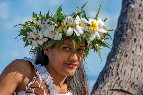 Young woman with flower wreath from Frangipani leaning on palm trunk