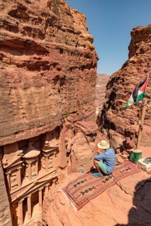 Tourist sits on a carpet and looks from above into the gorge Siq