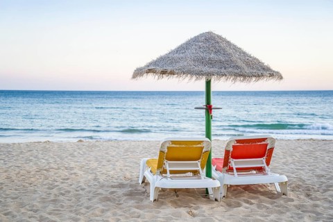 Colorful red and yellow sun beds under straw umbrellas on Falesia Beach