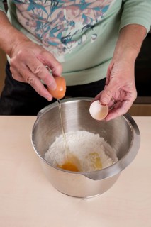 Woman putting egg in bowl of dough