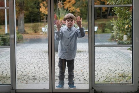 Child squeezes nose and hands on glass panel