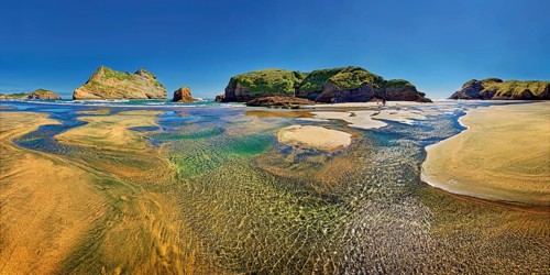 Sandy beach with receding water and rocky island in the surf