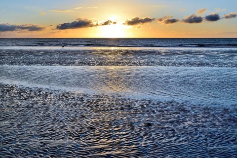 Sunset on sandy beach with wave-like structures