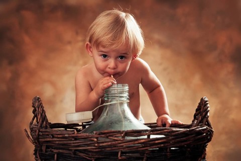 Three year-old girl drinking through a straw from glass carboy