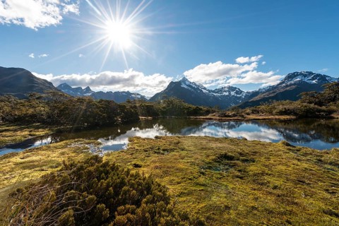 Sun shining on small mountain lake with reflection of a mountain chain