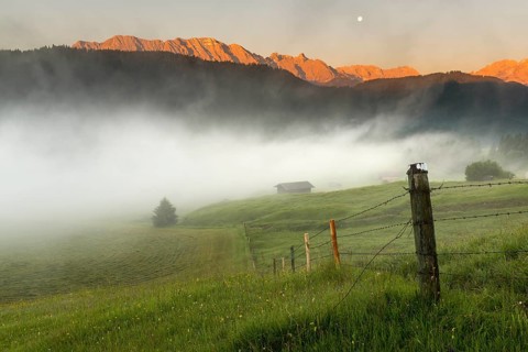 Pasture fence on mountain meadow with small cabin in the fog
