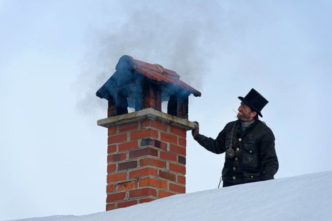 Chimney sweeper in winter on a roof with smoky chimney