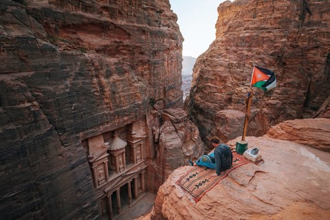 Tourist sits at the edge of a rock and looks from above into the canyon Siq