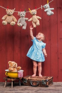 Three year-old girl reaching for teddy bears on clothesline