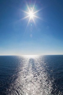 Ship's wake and sunburst over shimmering Mediterranean sea in late afternoon off the coast of Italy