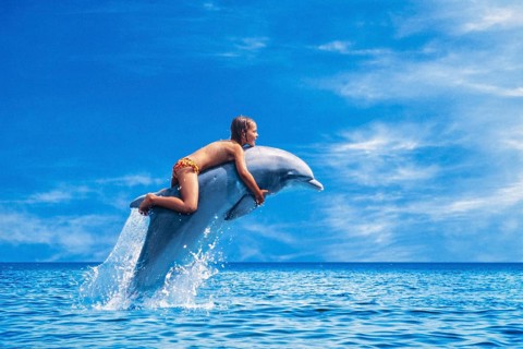 Six year old girl riding a dolphin leaping out of the sea