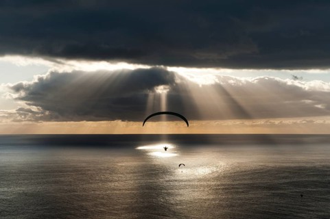 Sun shines behind dark clouds with paraglider over the Atlantic