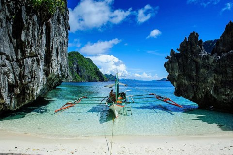 Outrigger boat on a little white beach and crystal clear water in the Bacuit archipelago