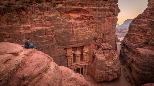 Tourist sits at the edge of a rock and looks from above into the canyon Siq