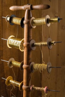 Thread stand in front of wooden wall with various gold and yellow yarns