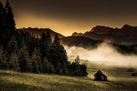Small cabin on mountain meadow at forest edge