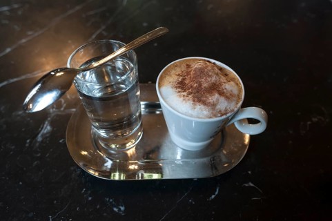 Cappuccino with cocoa powder and glass of water on marble table