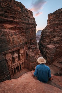 Tourist sits at the edge of a rock and looks from above into the canyon Siq