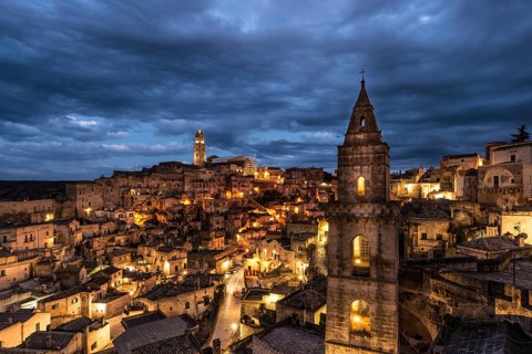 Church tower San Pietro Barisano in front of illuminated old town with cathedral