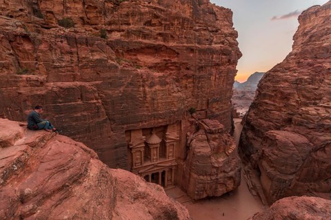 Tourist sits at the edge of a rock and looks from above into the canyon Siq