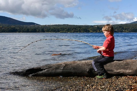 Small boy sitting on a tree trunk fishing at Lake Nahuel Huapi