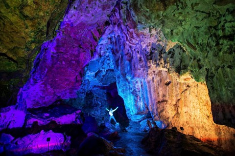 Young man in a colourfully illuminated stalactite cave