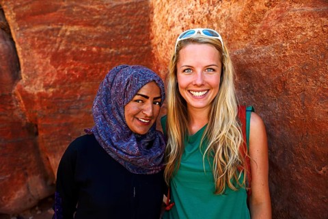 Tourist girl poses with local bedouin girl at colourful rock-formations in Petra