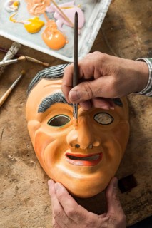 Painting the face of a wooden mask with a paintbrush