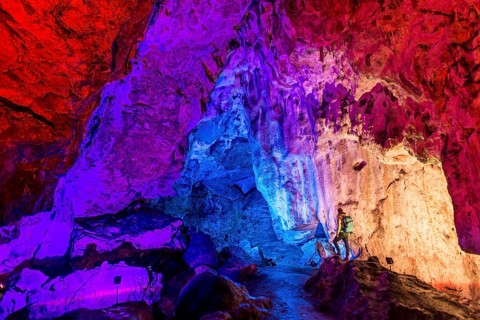 Man in a colourfully illuminated stalactite cave with stalagmites and stalactites