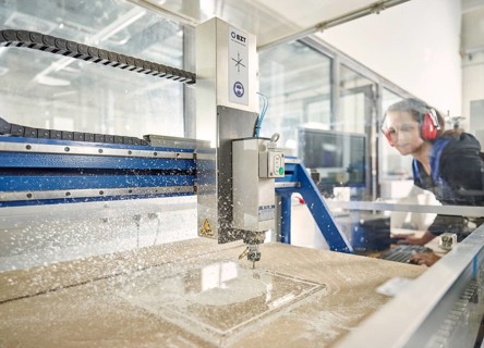 Woman with ear protection operates CNC milling machine
