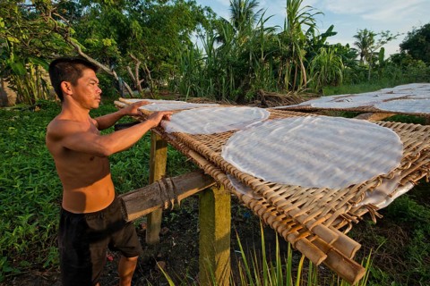 Vietnamese worker spreads steaming rice noodle patties on bamboo frame to dry